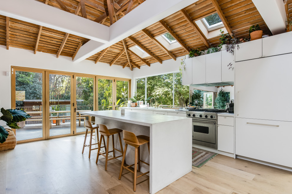 Inspiration for a midcentury kitchen in Los Angeles with flat-panel cabinets, white cabinets, concrete benchtops, light hardwood floors, with island and white benchtop.