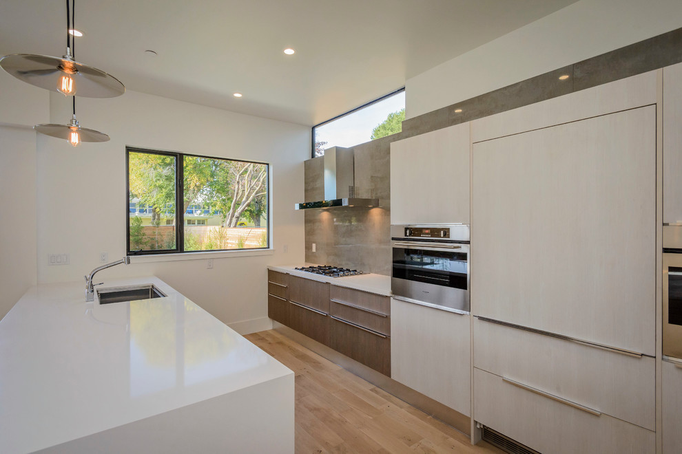 This is an example of a mid-sized modern galley open plan kitchen in San Francisco with a drop-in sink, flat-panel cabinets, light wood cabinets, quartz benchtops, brown splashback, stone tile splashback, white appliances, light hardwood floors and with island.