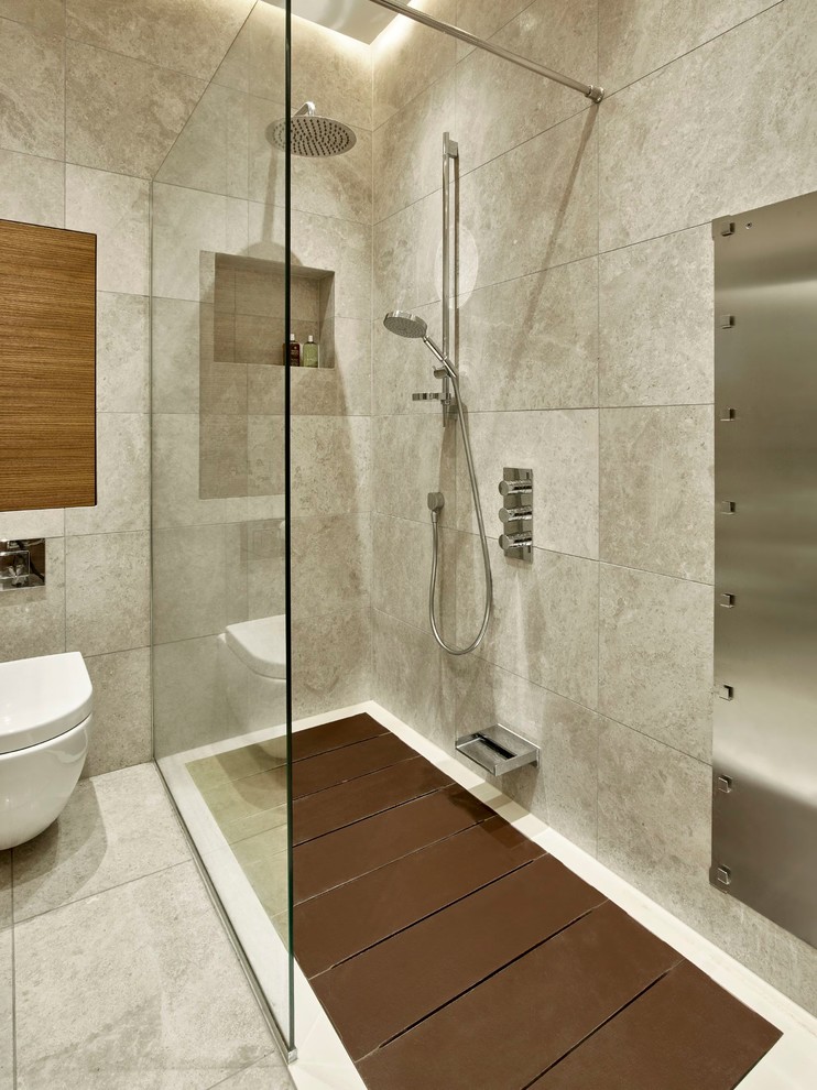 Design ideas for a modern bathroom in London with flat-panel cabinets, dark wood cabinets, a drop-in tub, a shower/bathtub combo, a wall-mount toilet, gray tile, porcelain tile, porcelain floors and a wall-mount sink.
