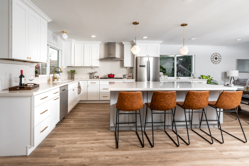 Design ideas for a large transitional l-shaped eat-in kitchen in San Diego with an undermount sink, shaker cabinets, white cabinets, quartz benchtops, white splashback, stainless steel appliances, porcelain floors, with island, brown floor and white benchtop.