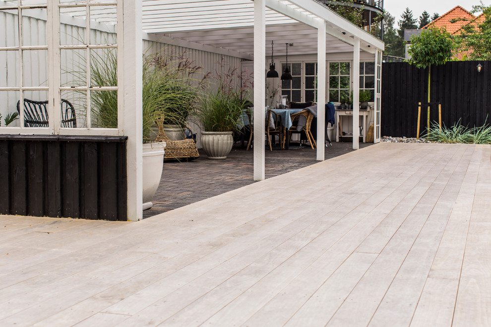 Large transitional backyard deck in Copenhagen with a pergola.