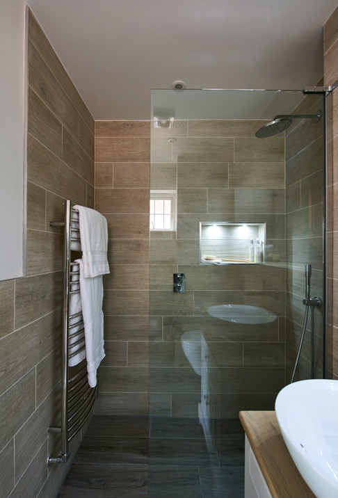 This is an example of a small contemporary master bathroom in Hertfordshire with furniture-like cabinets, white cabinets, an open shower, a wall-mount toilet, beige tile, porcelain tile, porcelain floors, a console sink, wood benchtops, beige floor and an open shower.