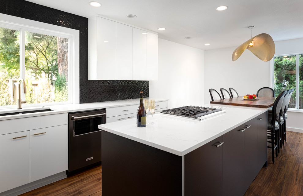 Design ideas for a mid-sized contemporary l-shaped open plan kitchen in Portland with an undermount sink, flat-panel cabinets, white cabinets, quartz benchtops, black splashback, ceramic splashback, black appliances, vinyl floors, with island and brown floor.