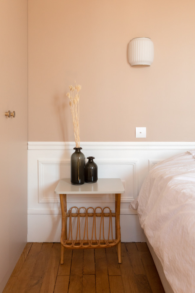 Exemple d'une chambre parentale haussmannienne et blanche et bois moderne de taille moyenne avec un mur rose, un sol en bois brun, une cheminée standard, un manteau de cheminée en pierre et un sol marron.