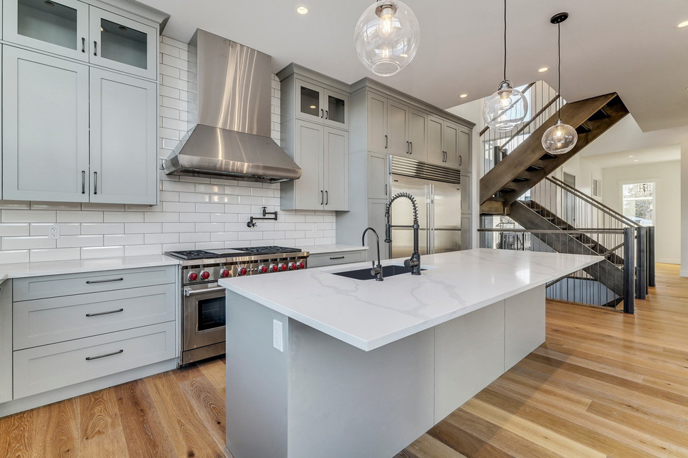 Example of a mid-sized transitional l-shaped medium tone wood floor and brown floor eat-in kitchen design in Calgary with a single-bowl sink, shaker cabinets, gray cabinets, quartzite countertops, white backsplash, ceramic backsplash, stainless steel appliances, an island and white countertops