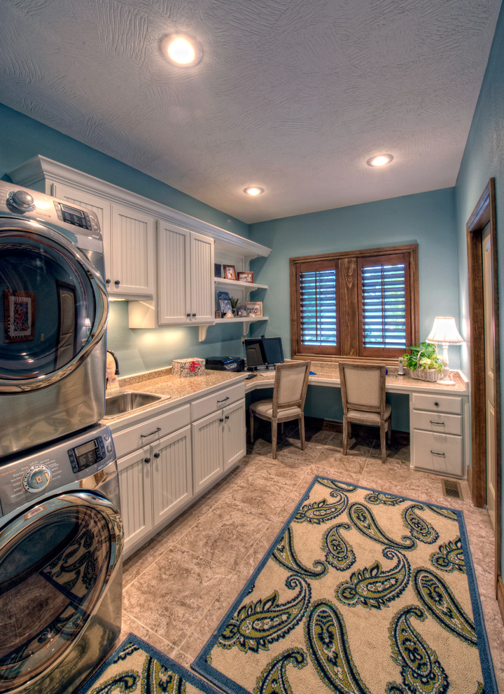 Design ideas for a large traditional l-shaped utility room in Other with a drop-in sink, white cabinets, granite benchtops, blue walls, porcelain floors, a stacked washer and dryer and recessed-panel cabinets.