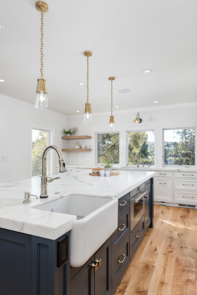 This is an example of a large country u-shaped open plan kitchen in San Francisco with a farmhouse sink, white cabinets, marble benchtops, white splashback, ceramic splashback, panelled appliances, medium hardwood floors, with island, brown floor, white benchtop and shaker cabinets.