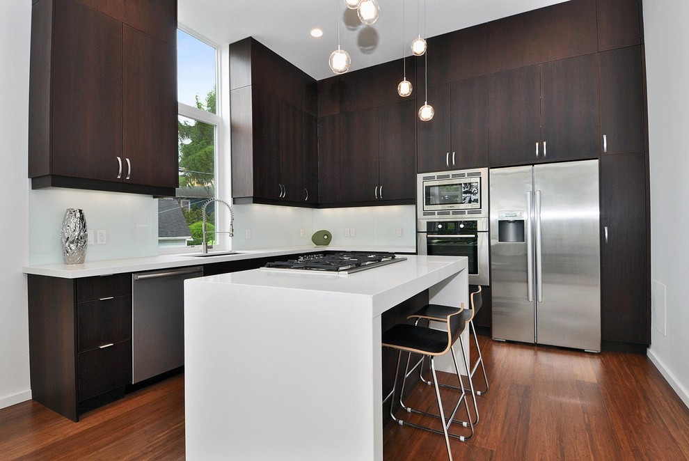 Photo of a mid-sized modern l-shaped separate kitchen in Seattle with stainless steel appliances, flat-panel cabinets, dark wood cabinets, solid surface benchtops, with island, an undermount sink, white splashback, medium hardwood floors and glass sheet splashback.