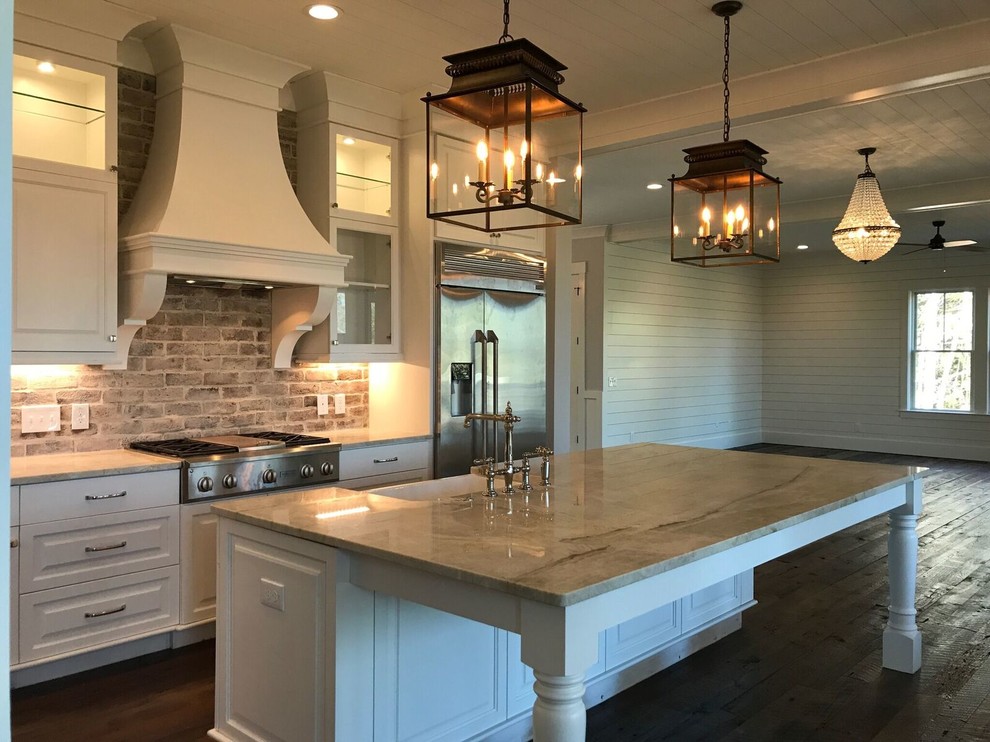 Design ideas for a mid-sized country l-shaped open plan kitchen in Charleston with a farmhouse sink, raised-panel cabinets, white cabinets, marble benchtops, brown splashback, brick splashback, stainless steel appliances, dark hardwood floors, with island and brown floor.