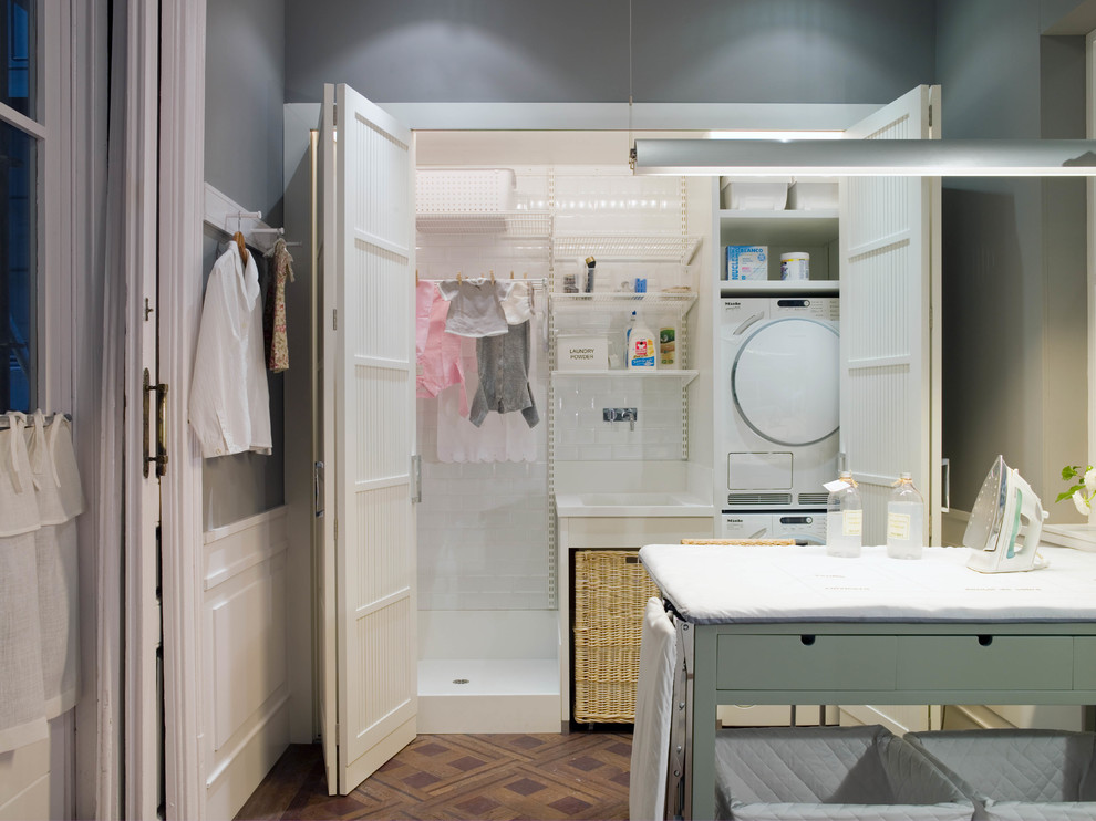 Mid-sized mediterranean dedicated laundry room in Barcelona with shaker cabinets, white cabinets, grey walls, medium hardwood floors and a stacked washer and dryer.