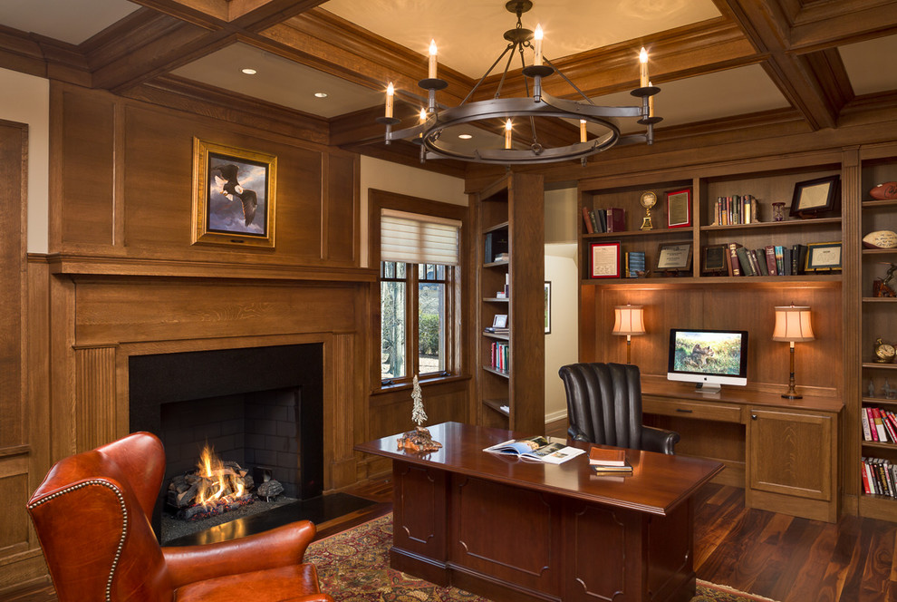 Design ideas for a large traditional home office in Other with brown walls, dark hardwood floors, a standard fireplace, a wood fireplace surround, a freestanding desk and brown floor.