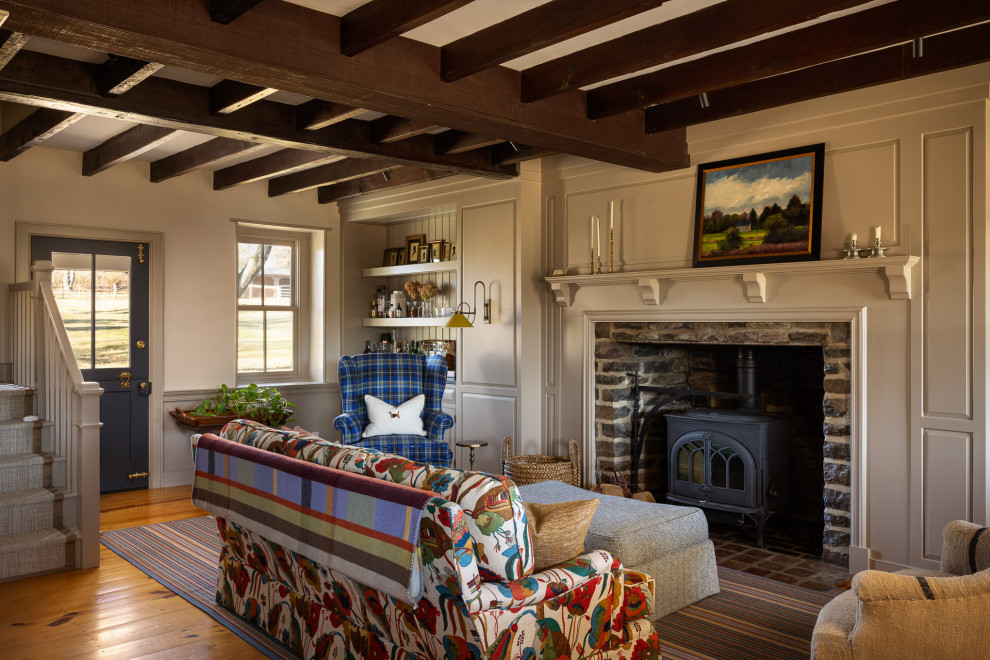 Cottage medium tone wood floor, brown floor, exposed beam and wall paneling living room photo in Philadelphia with beige walls and a wood stove