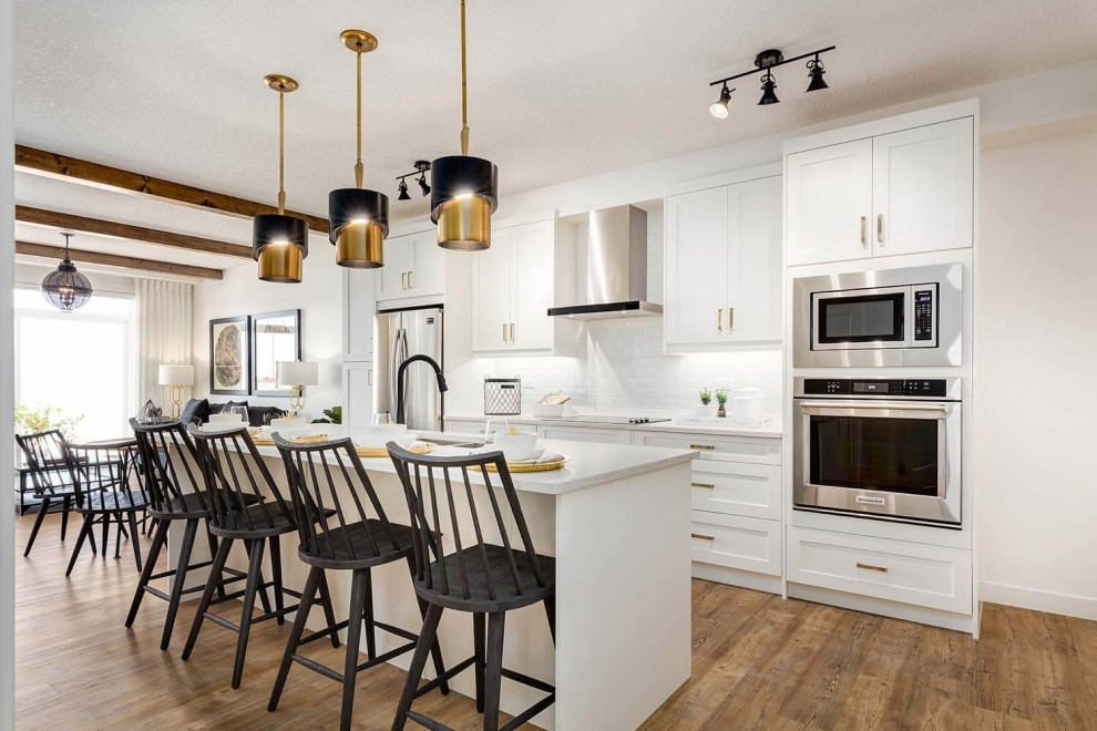 Mid-sized transitional galley eat-in kitchen in Calgary with an undermount sink, shaker cabinets, white cabinets, quartz benchtops, white splashback, subway tile splashback, stainless steel appliances, medium hardwood floors, with island, brown floor and grey benchtop.