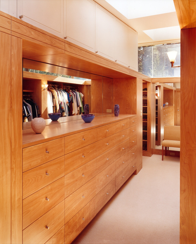 This is an example of a mid-sized modern gender-neutral walk-in wardrobe in Boston with flat-panel cabinets, medium wood cabinets and carpet.