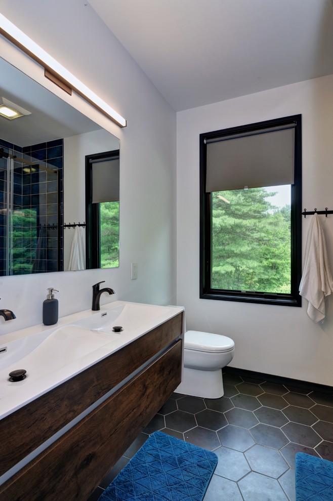 Mid-sized transitional kids bathroom in Other with flat-panel cabinets, medium wood cabinets, an alcove tub, a shower/bathtub combo, a one-piece toilet, blue tile, ceramic tile, white walls, ceramic floors, an integrated sink, solid surface benchtops, black floor, a sliding shower screen and white benchtops.