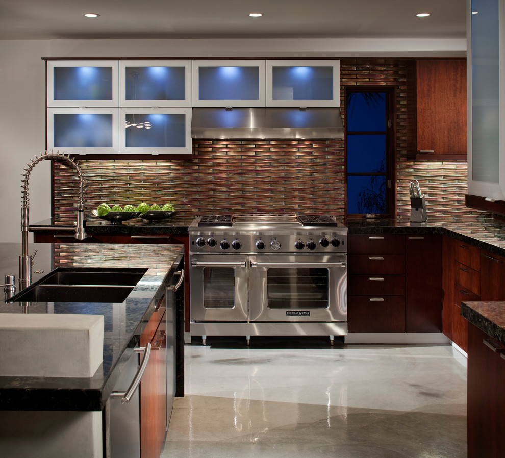 This is an example of a mid-sized contemporary u-shaped open plan kitchen in Los Angeles with a double-bowl sink, flat-panel cabinets, dark wood cabinets, granite benchtops, metallic splashback, glass tile splashback, stainless steel appliances and concrete floors.