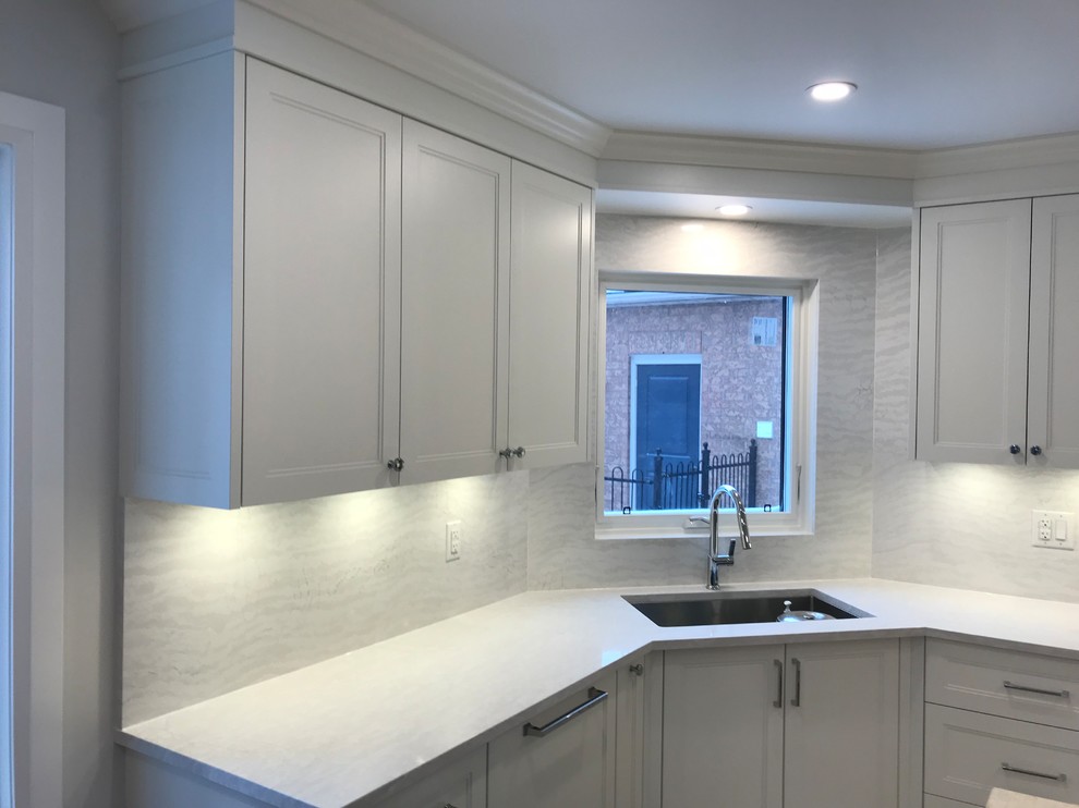 Inspiration for a mid-sized timeless u-shaped light wood floor kitchen pantry remodel in Toronto with an undermount sink, recessed-panel cabinets, white cabinets, solid surface countertops, white backsplash, stone slab backsplash, stainless steel appliances, an island and white countertops