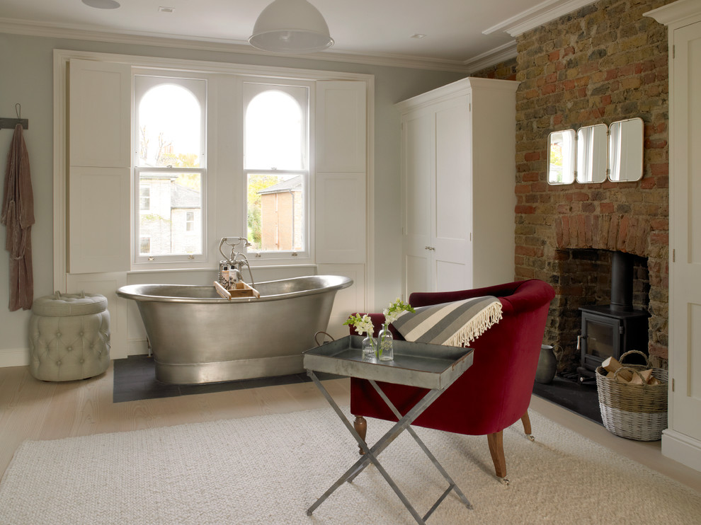 This is an example of an expansive traditional bathroom in London with a freestanding tub, light hardwood floors, white walls and beige floor.