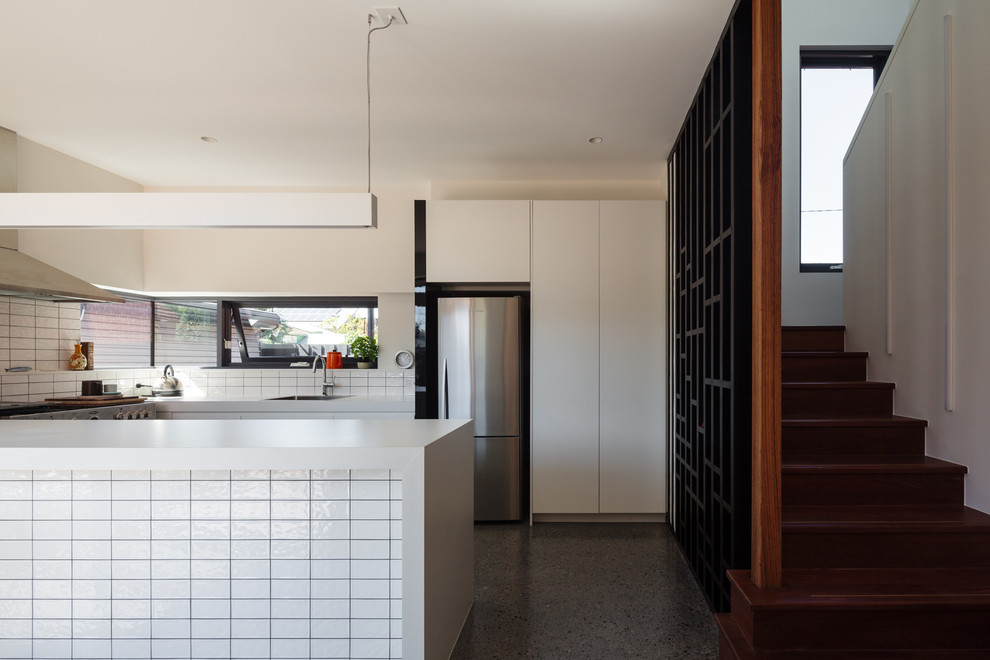 This is an example of a contemporary u-shaped kitchen in Melbourne with an undermount sink, flat-panel cabinets, white cabinets, white splashback, stainless steel appliances, concrete floors, a peninsula, grey floor and white benchtop.