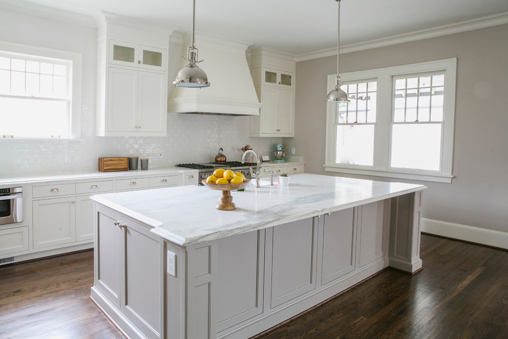Photo of an arts and crafts open plan kitchen in Atlanta with a farmhouse sink, flat-panel cabinets, white cabinets, white splashback, ceramic splashback, stainless steel appliances, dark hardwood floors and with island.