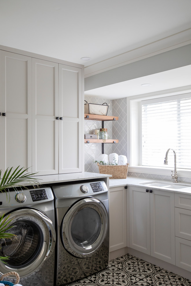 This is an example of a country u-shaped dedicated laundry room in Vancouver with an undermount sink, shaker cabinets, quartzite benchtops, grey walls, ceramic floors, a side-by-side washer and dryer, grey cabinets, multi-coloured floor and white benchtop.