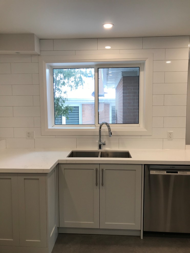 Home design - mid-sized transitional porcelain tile and brown floor home design idea in Toronto with an undermount sink, shaker cabinets, gray cabinets, quartz countertops, white backsplash, subway tile backsplash, stainless steel appliances, an island and white countertops