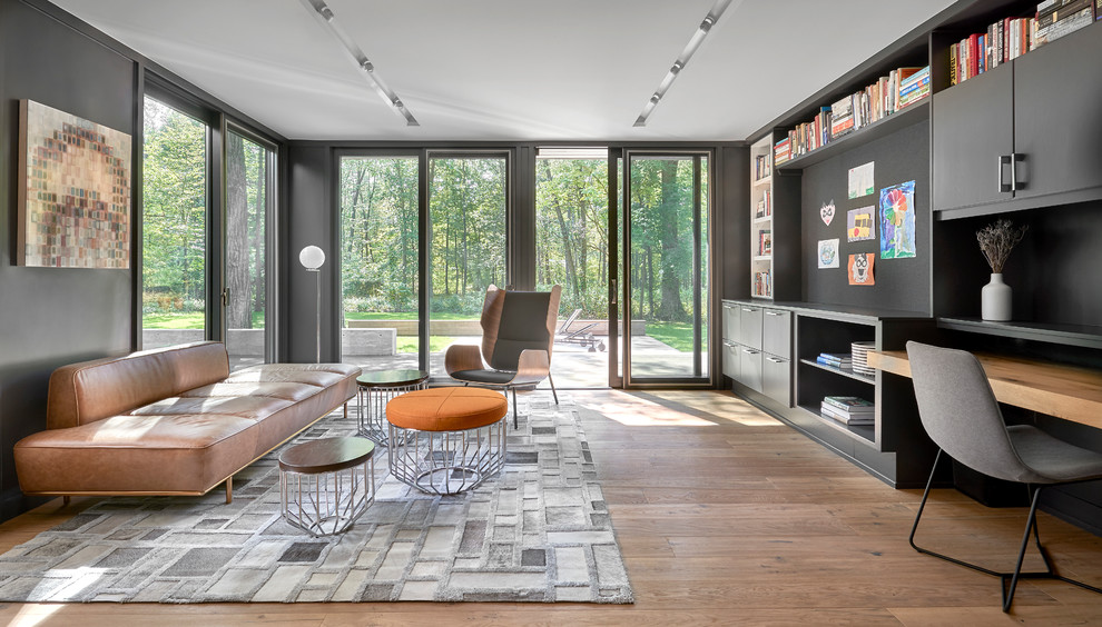 This is an example of a large contemporary home office in Chicago with light hardwood floors, a built-in desk, a library and black walls.