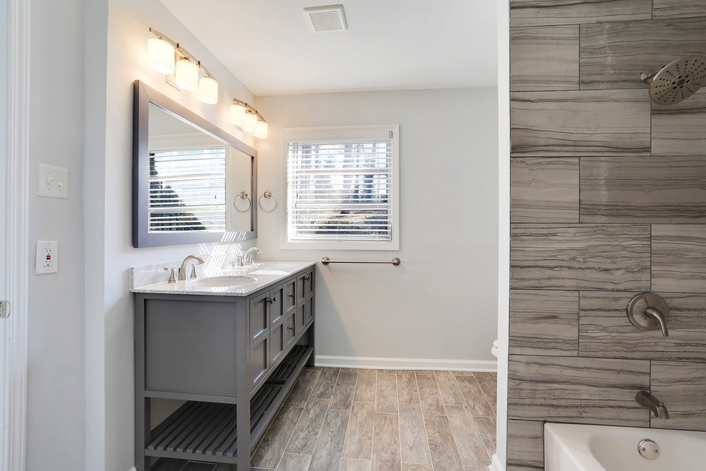 This is an example of a mid-sized midcentury master bathroom in Atlanta with furniture-like cabinets, medium wood cabinets, a drop-in tub, a shower/bathtub combo, gray tile, ceramic tile, grey walls, porcelain floors and soapstone benchtops.