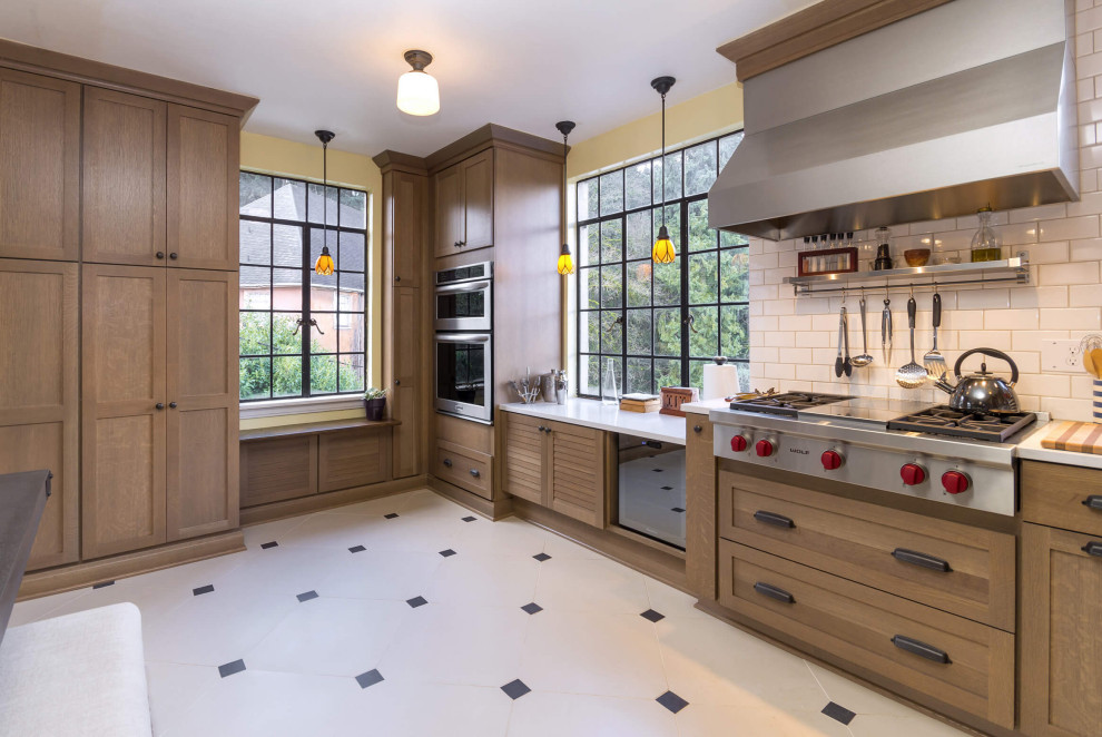 Example of a transitional l-shaped porcelain tile and white floor enclosed kitchen design in Portland with an undermount sink, shaker cabinets, light wood cabinets, solid surface countertops, white backsplash, ceramic backsplash, stainless steel appliances, an island and white countertops