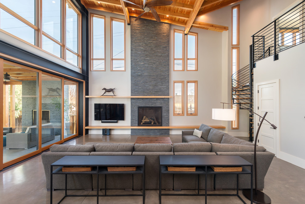This is an example of a large country open concept family room in San Francisco with grey walls, concrete floors, a standard fireplace, a stone fireplace surround and a wall-mounted tv.