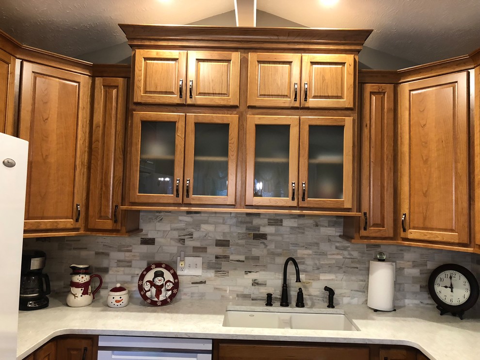 Inspiration for a mid-sized transitional u-shaped laminate floor and brown floor eat-in kitchen remodel in Omaha with an undermount sink, raised-panel cabinets, medium tone wood cabinets, quartz countertops, beige backsplash, stone tile backsplash, white appliances and white countertops