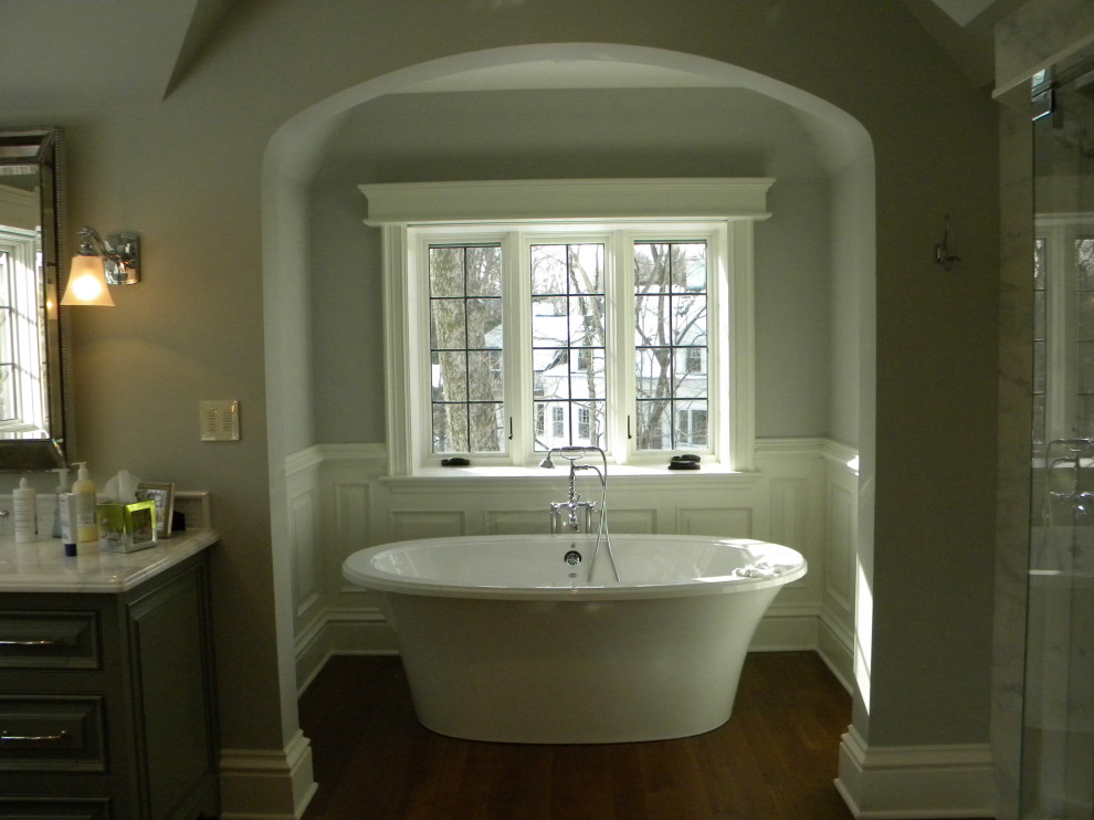 На фото: большая главная ванная комната в классическом стиле с фасадами с выступающей филенкой, зелеными фасадами, отдельно стоящей ванной, двойным душем, унитазом-моноблоком, белой плиткой, мраморной плиткой, серыми стенами, паркетным полом среднего тона, врезной раковиной, мраморной столешницей, коричневым полом, душем с распашными дверями, белой столешницей, сиденьем для душа, тумбой под две раковины, встроенной тумбой и панелями на стенах