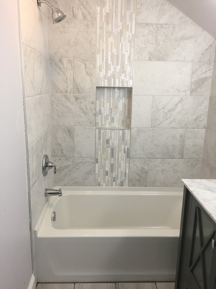 This is an example of a mid-sized modern kids bathroom in Milwaukee with glass-front cabinets, grey cabinets, a drop-in tub, an alcove shower, a two-piece toilet, gray tile, porcelain tile, grey walls, porcelain floors, an integrated sink, marble benchtops, grey floor and a shower curtain.