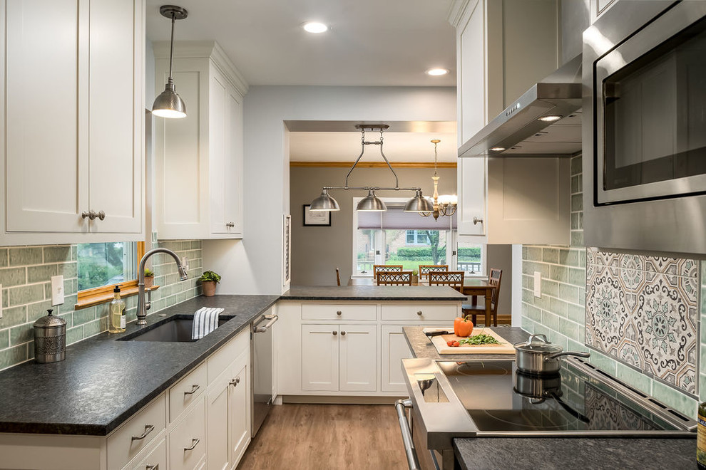 Example of a mid-sized transitional galley vinyl floor and brown floor eat-in kitchen design in Columbus with an undermount sink, shaker cabinets, white cabinets, granite countertops, green backsplash, ceramic backsplash, stainless steel appliances, a peninsula and black countertops