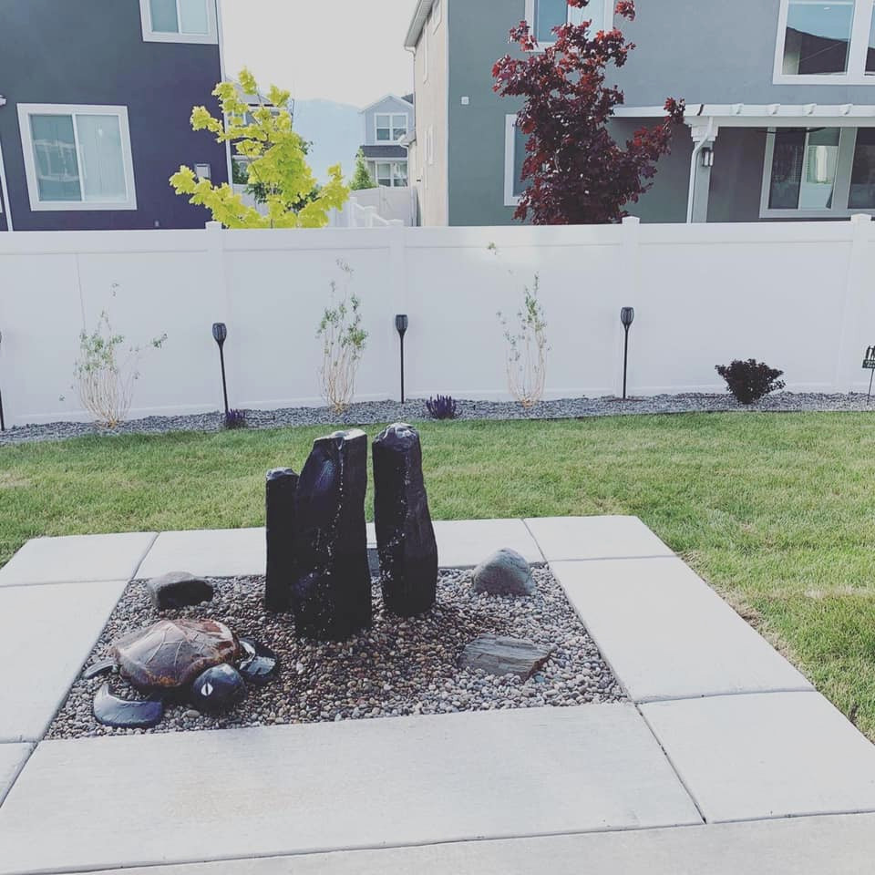This is an example of a small modern backyard full sun xeriscape for summer in Salt Lake City with a fire feature, river rock and a vinyl fence.