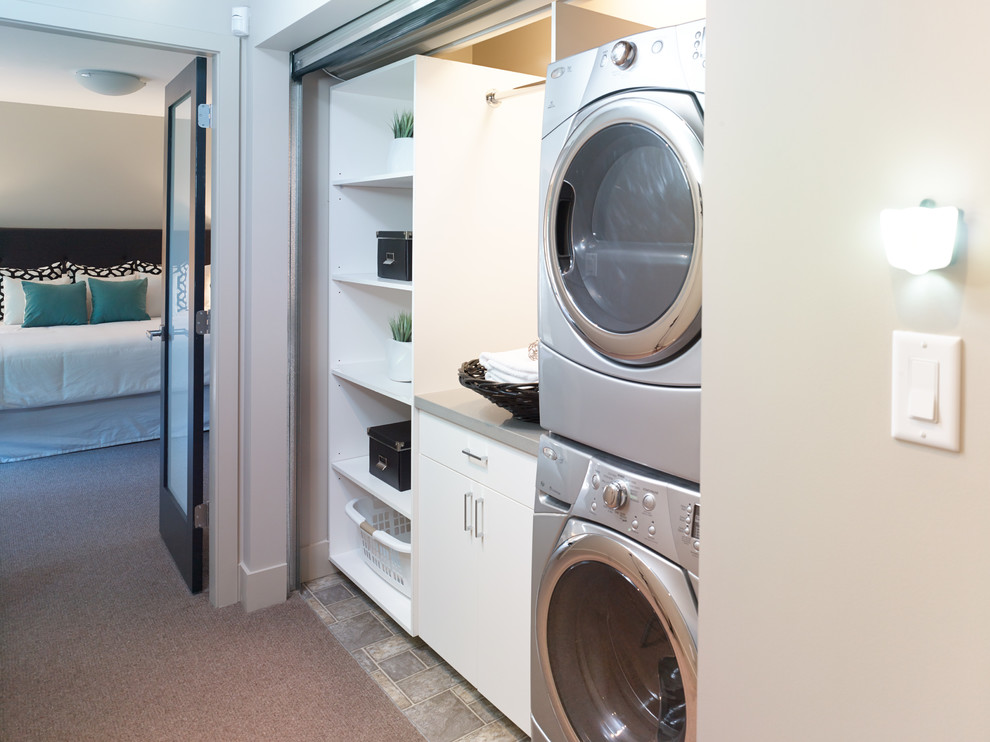 This is an example of a small contemporary dedicated laundry room in Vancouver with flat-panel cabinets, white cabinets and a stacked washer and dryer.