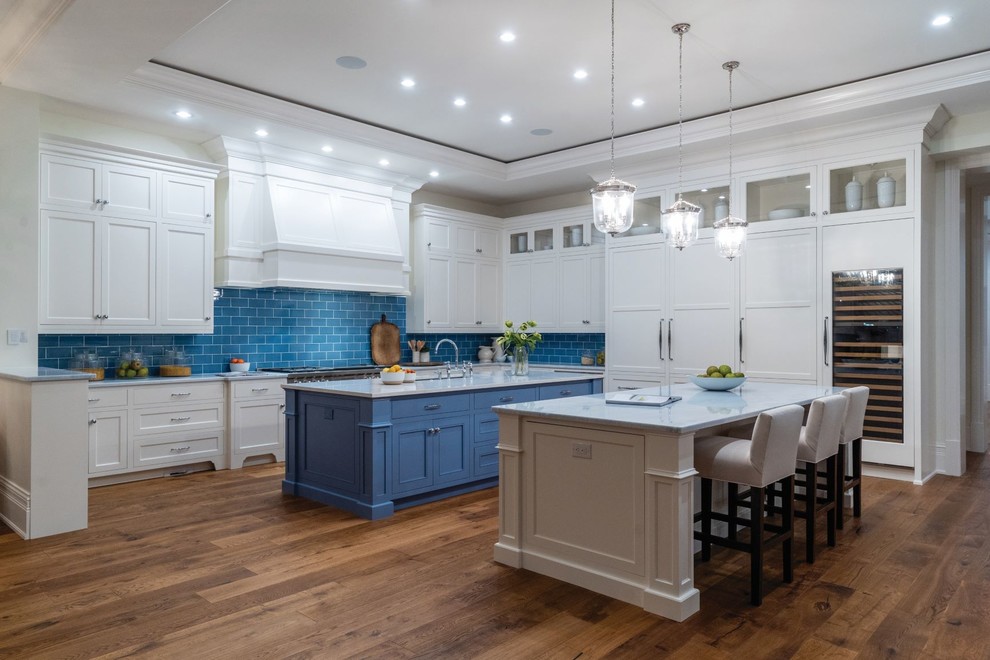 Photo of an expansive traditional kitchen in Miami with an undermount sink, recessed-panel cabinets, white cabinets, onyx benchtops, blue splashback, porcelain splashback, panelled appliances, medium hardwood floors, multiple islands and blue benchtop.