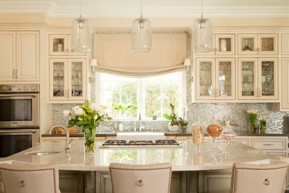 Elegant kitchen photo in Los Angeles with a farmhouse sink, beaded inset cabinets, beige cabinets, metallic backsplash, mosaic tile backsplash, stainless steel appliances and beige countertops
