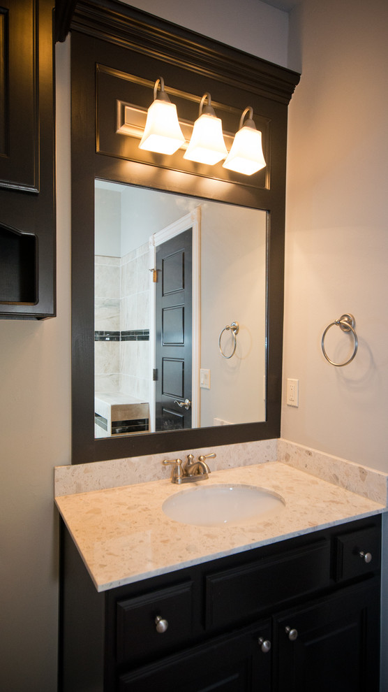 Inspiration for a mid-sized transitional bathroom in Oklahoma City with a drop-in sink, raised-panel cabinets, dark wood cabinets, glass benchtops, a one-piece toilet, brown tile, ceramic tile, grey walls and ceramic floors.
