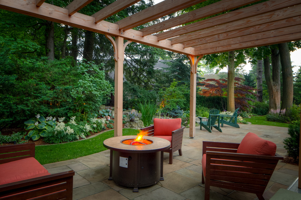 This is an example of a large traditional backyard patio in Toronto with a fire feature, a pergola and natural stone pavers.
