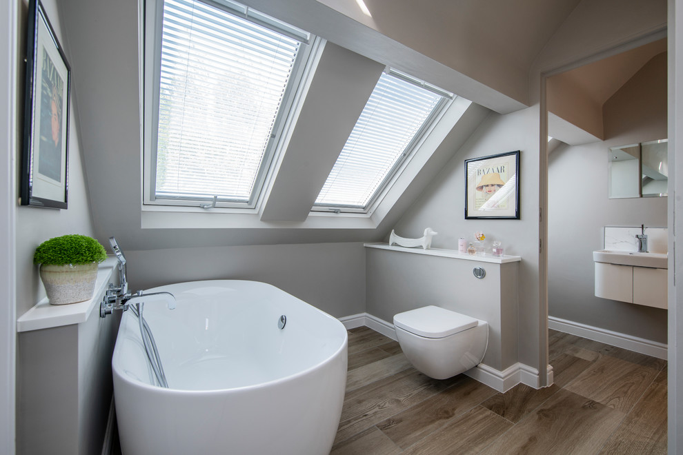 Photo of a small contemporary bathroom in Surrey with a freestanding tub, a wall-mount toilet, grey walls, dark hardwood floors, a wall-mount sink and brown floor.