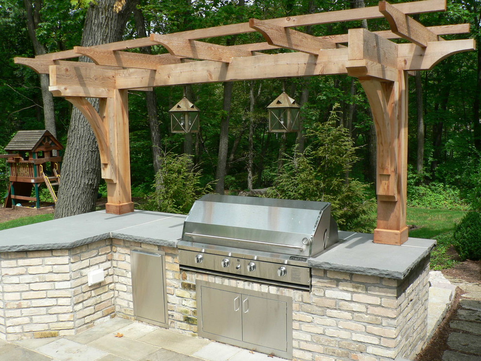 This is an example of a small traditional backyard patio in Milwaukee with an outdoor kitchen, natural stone pavers and a pergola.