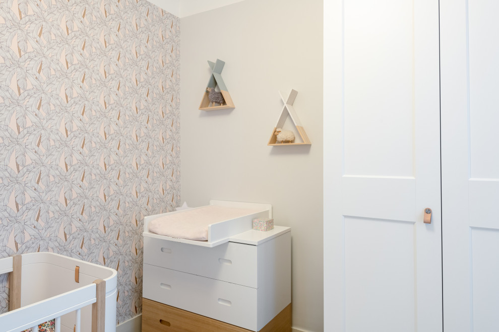 Design ideas for a small contemporary nursery for girls in Paris with beige walls, light hardwood flooring and wallpapered walls.