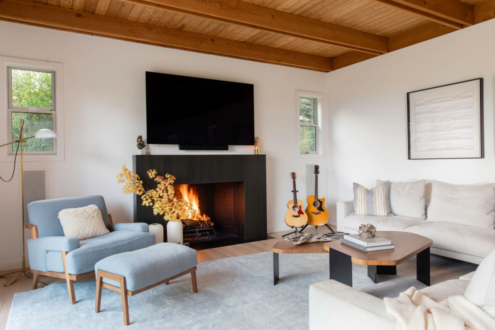 Photo of a mid-sized beach style open concept family room in San Francisco with white walls, a standard fireplace, a stone fireplace surround, a wall-mounted tv, beige floor and wood.