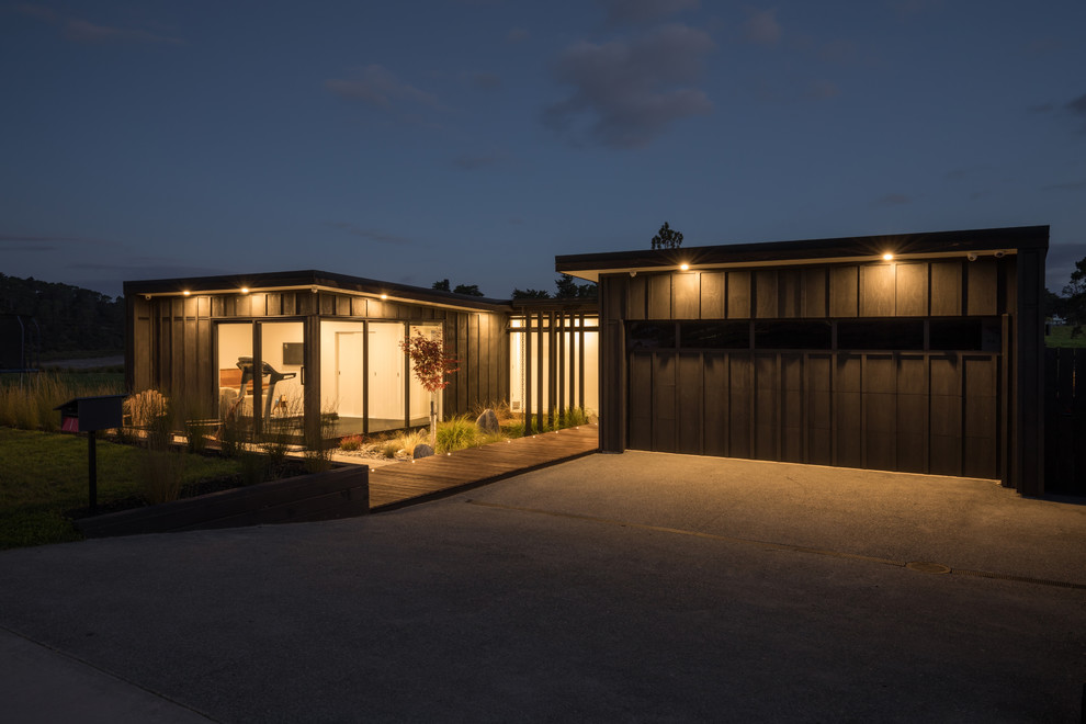 This is an example of a mid-sized contemporary one-storey black house exterior in Auckland with wood siding, a flat roof and a metal roof.