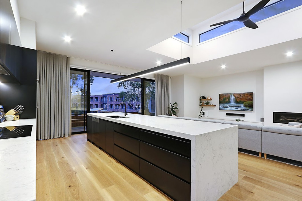 Design ideas for a mid-sized modern galley open plan kitchen in Melbourne with an undermount sink, flat-panel cabinets, black cabinets, quartz benchtops, grey splashback, ceramic splashback, stainless steel appliances, light hardwood floors, with island, beige floor and white benchtop.