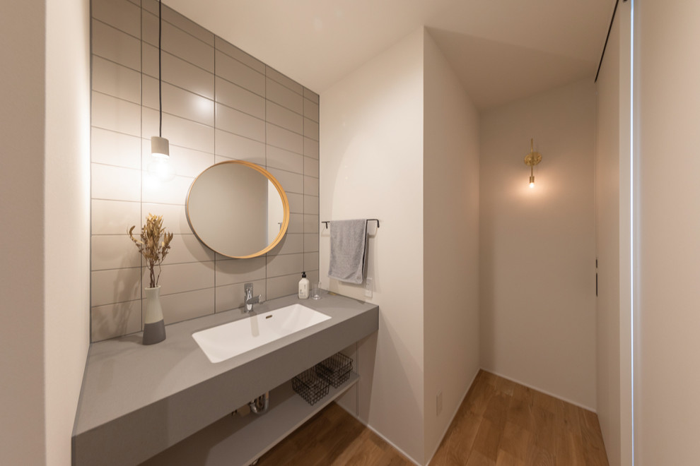 Inspiration för ett orientaliskt grå grått toalett, med öppna hyllor, grå skåp, vita väggar, mellanmörkt trägolv, ett undermonterad handfat, laminatbänkskiva och brunt golv