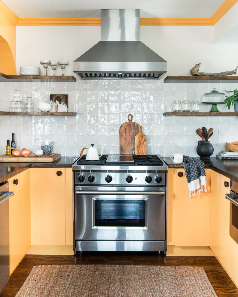 Mid-sized eclectic u-shaped separate kitchen in Chicago with a farmhouse sink, flat-panel cabinets, yellow cabinets, wood benchtops, white splashback, terra-cotta splashback, stainless steel appliances, medium hardwood floors, a peninsula, brown floor and brown benchtop.