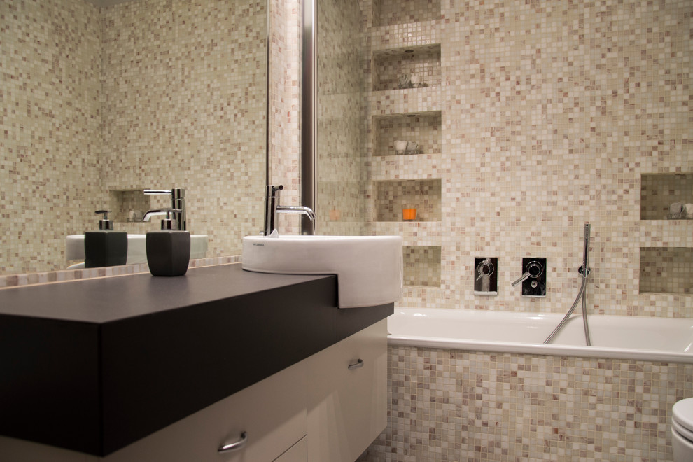 This is an example of a mid-sized contemporary master bathroom in Rome with flat-panel cabinets, white cabinets, an alcove tub, a shower/bathtub combo, a two-piece toilet, beige tile, mosaic tile, white walls, a vessel sink, solid surface benchtops, a hinged shower door, black benchtops, a niche, a single vanity, a floating vanity, recessed, cement tiles and grey floor.