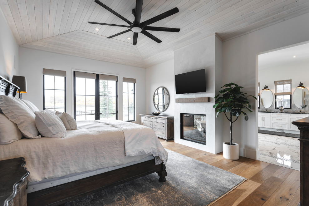 This is an example of a large master bedroom in Calgary with white walls, dark hardwood floors, a two-sided fireplace, a plaster fireplace surround and recessed.